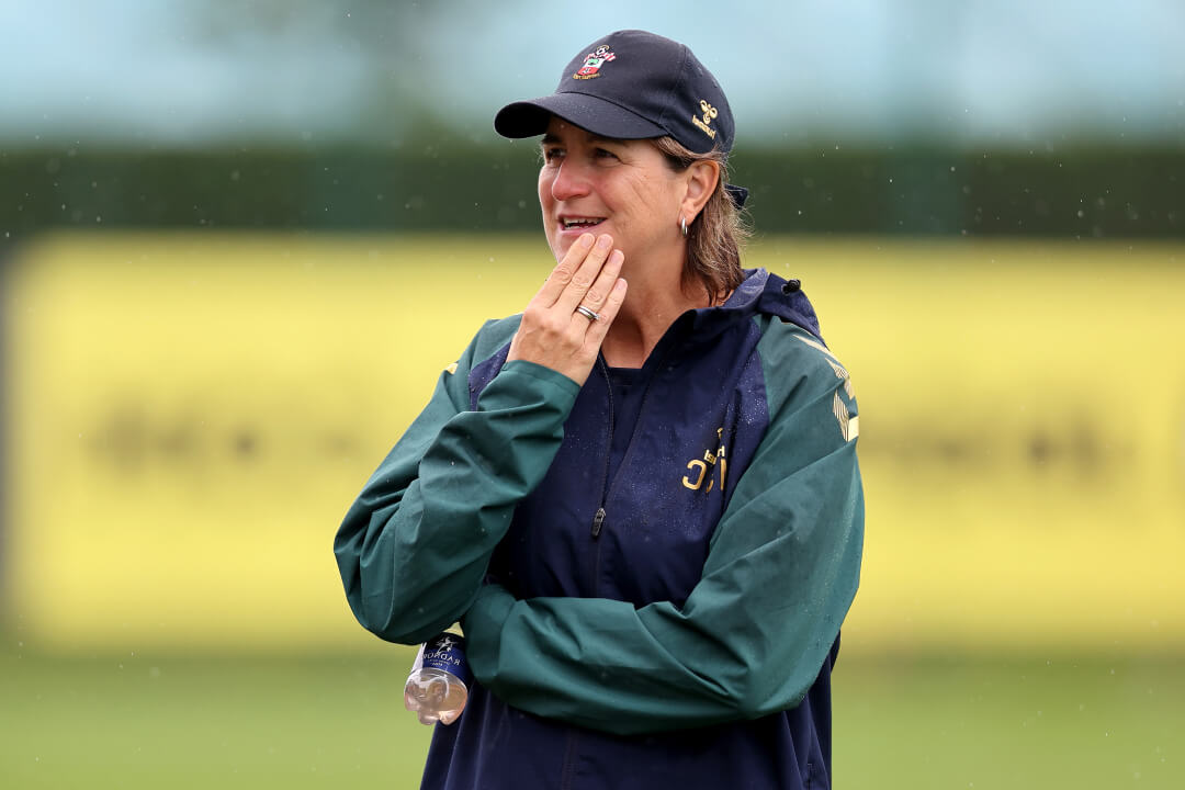 Image shows a female football coach with brown hair, wearing a waterproof jacket and a cap.