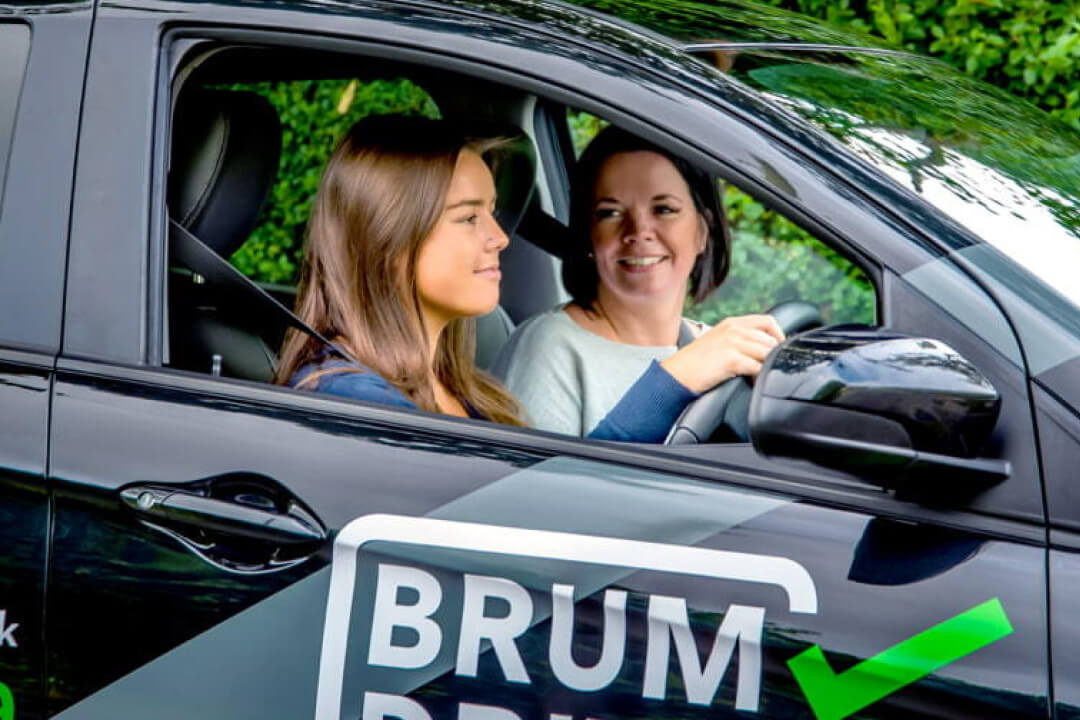 Driving instructor teaching a young woman in a black car with Brum Driving School logo on the side