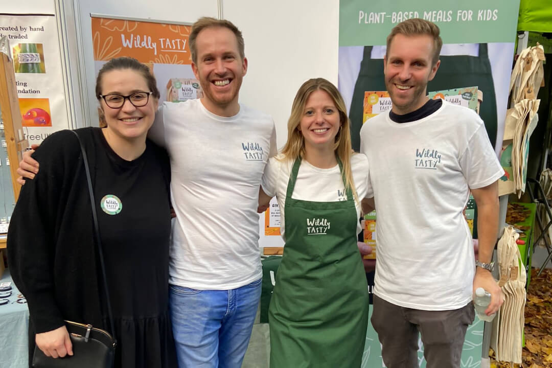 Four people, three of which are wearing tee shirts with the 'Wildly Tasty' logo on one side. They are at a food festival.