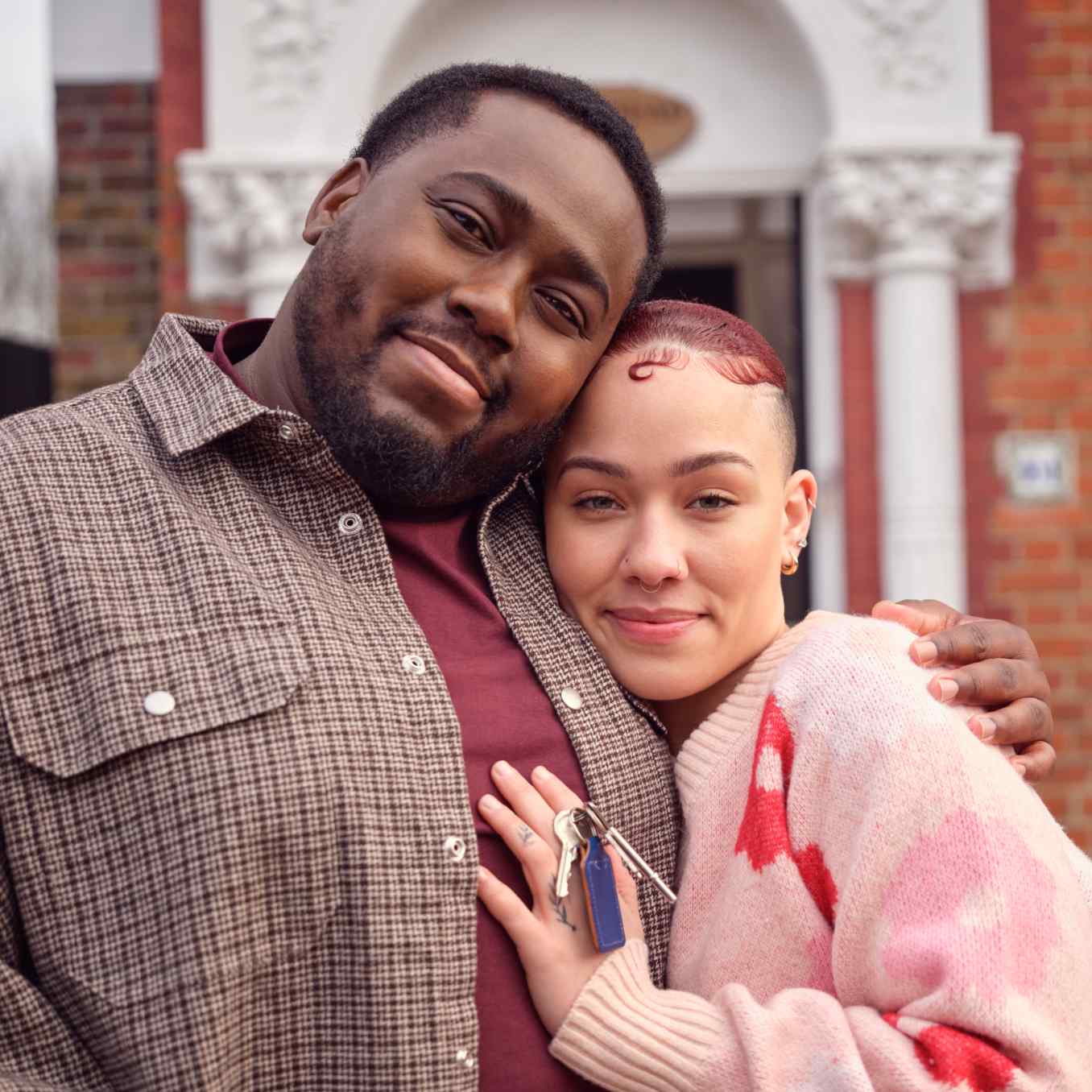 A couple standing outside a house, holding keys.