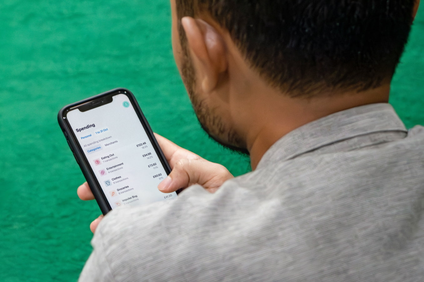 Man looking at his phone, which shows the Spending Insights tab of the Starling app.