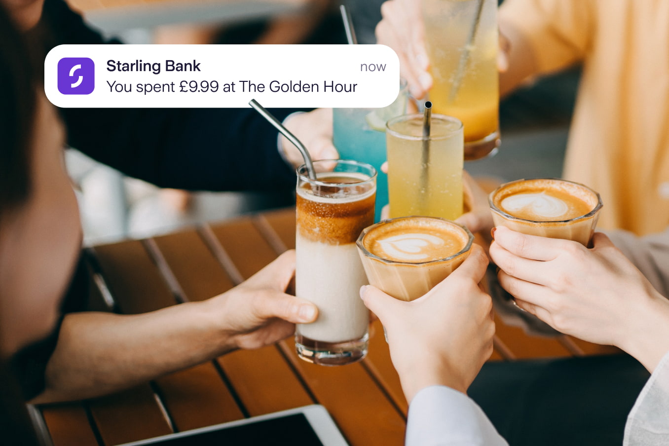 Four people with coffee and cold drinks clinking the glasses in a cheers. Notification from Starling reads that someone has spent £9.99 at The Golden Hour.