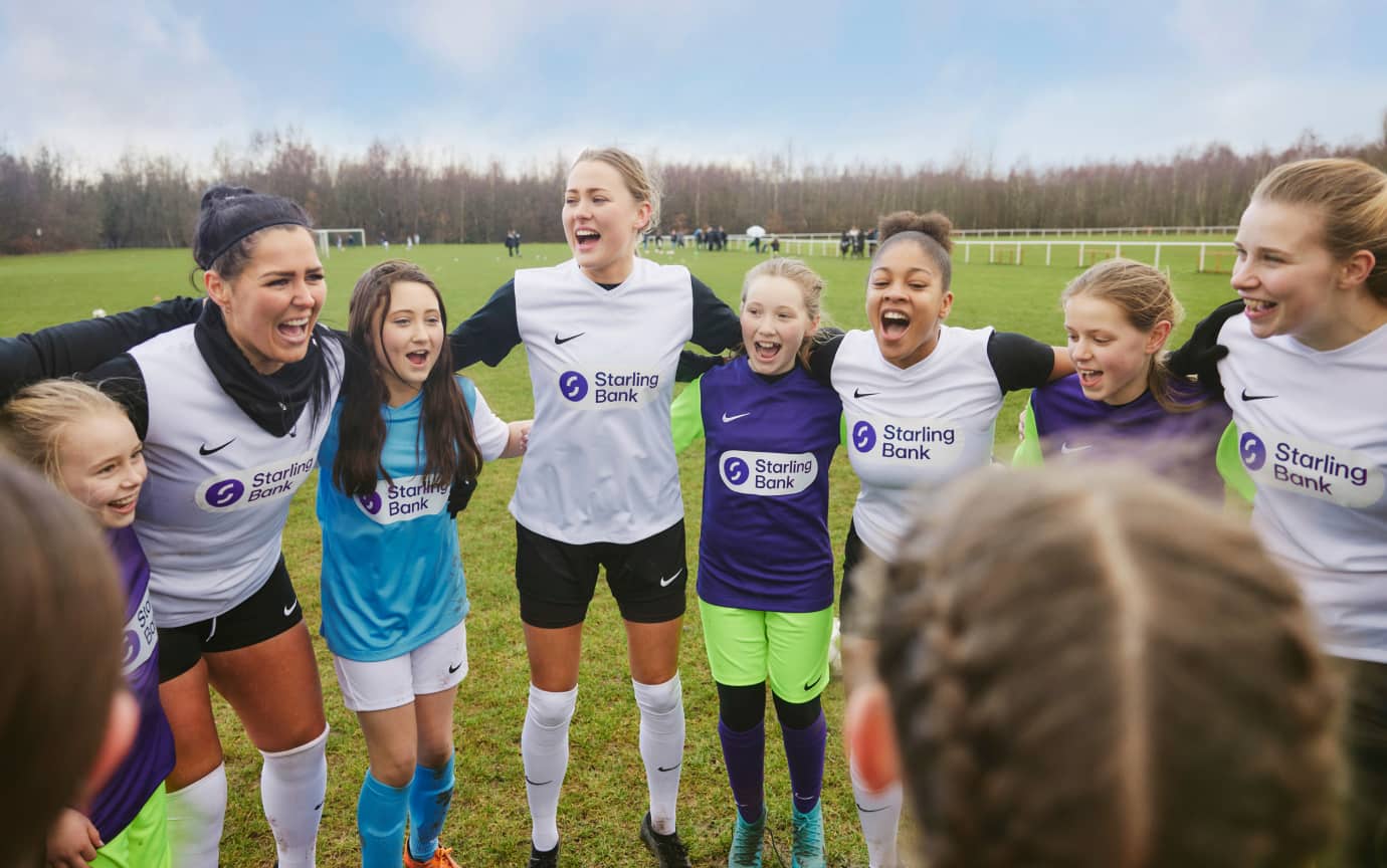 Astley & Tyldesley girls football team gathered in a huddle with older players
