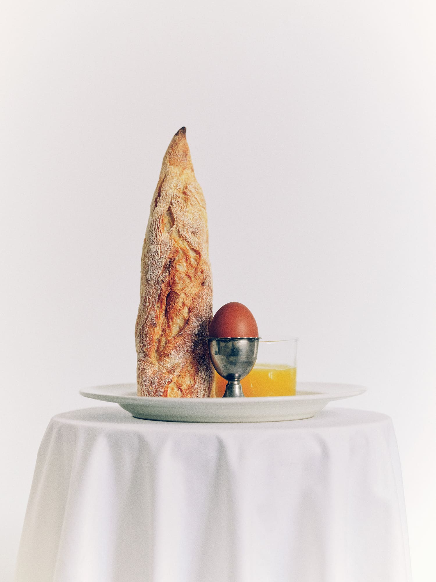 A baguette boiled egg and glass of juice arranged artfully