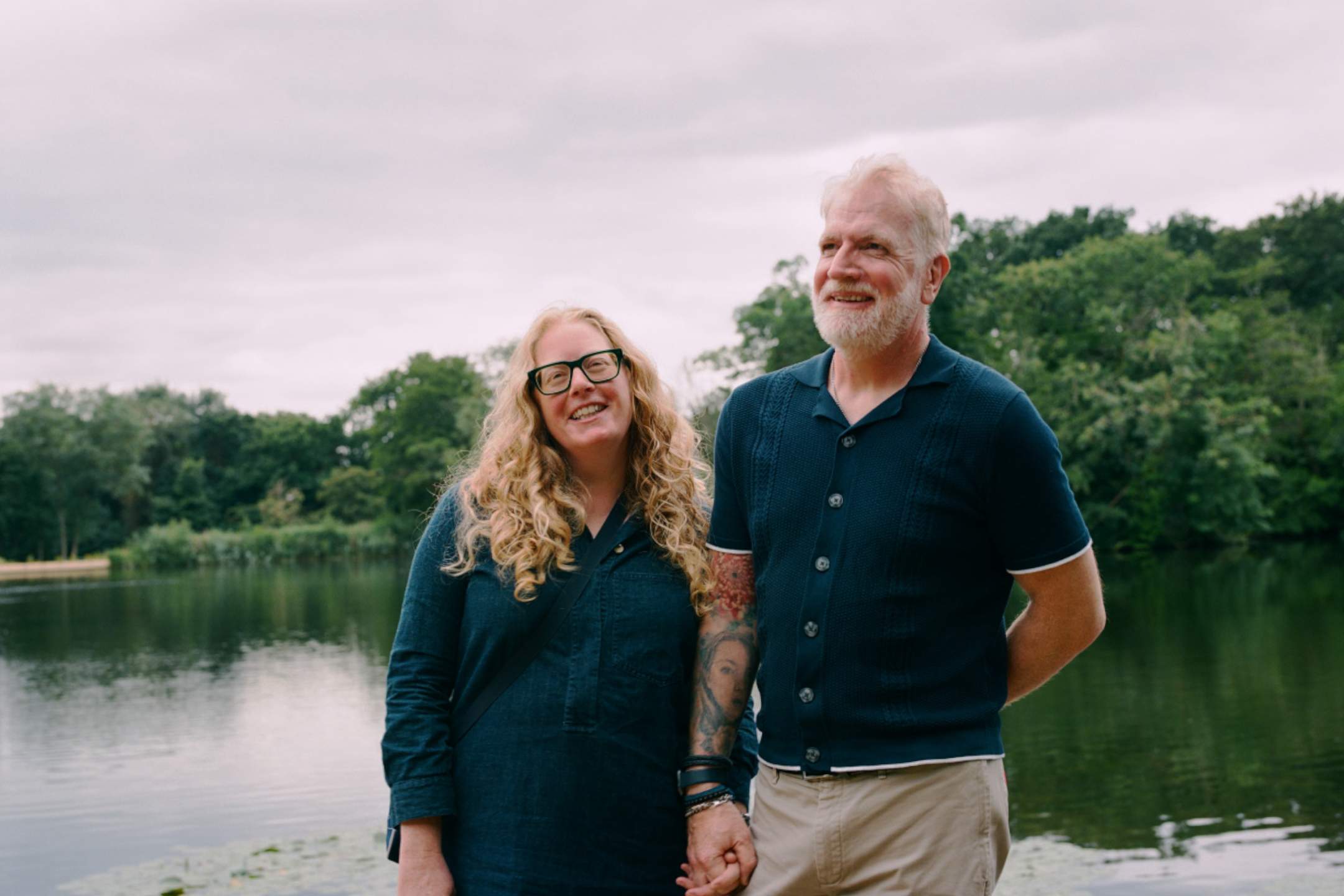 A couple holding hands, standing in front of a lake.