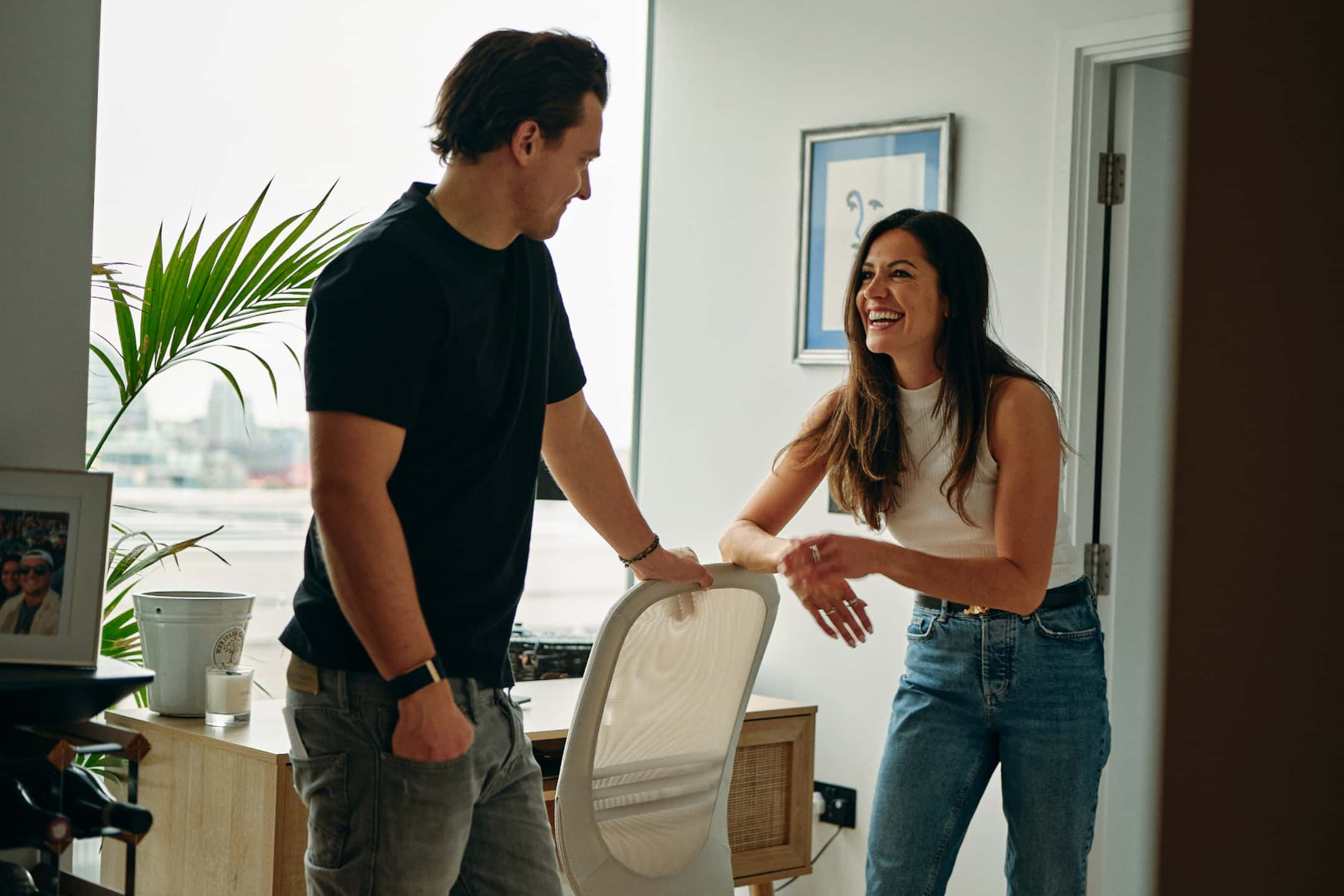 A couple is standing at their apartments, looking at each other and smiling.