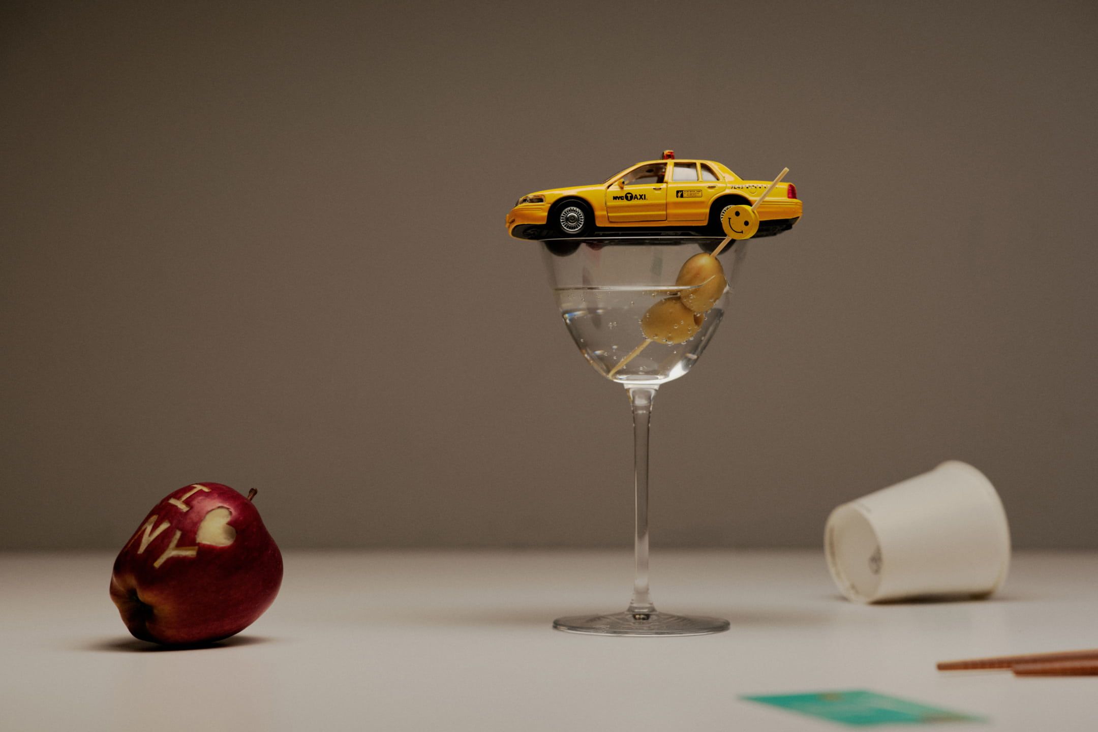 Still life image of a toy yellow taxi car on top of the cocktail glass