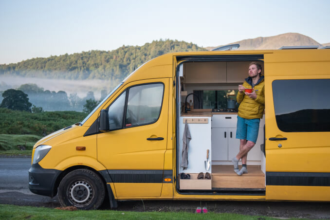 A man standing inside of the campervan having breakfast with a mountain view