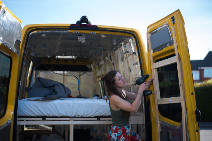 Woman screwing a frame on the back door of the campervan