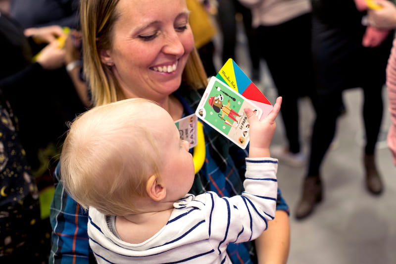 A mother holds a baby who is smiling with a book