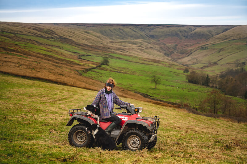 Dot sits with her dog, on her ATV, in the middle of a beautiful landscape.
