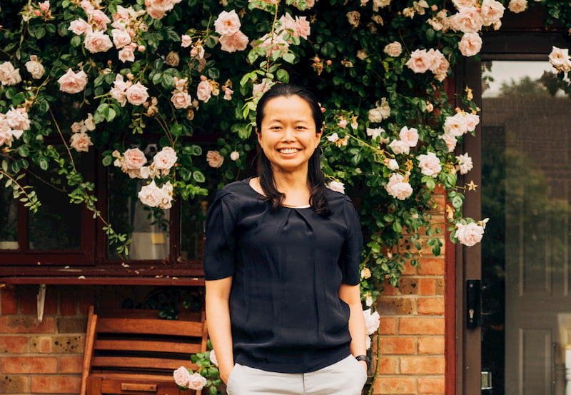 A woman smiling standing in front of a wall decorated with flowers